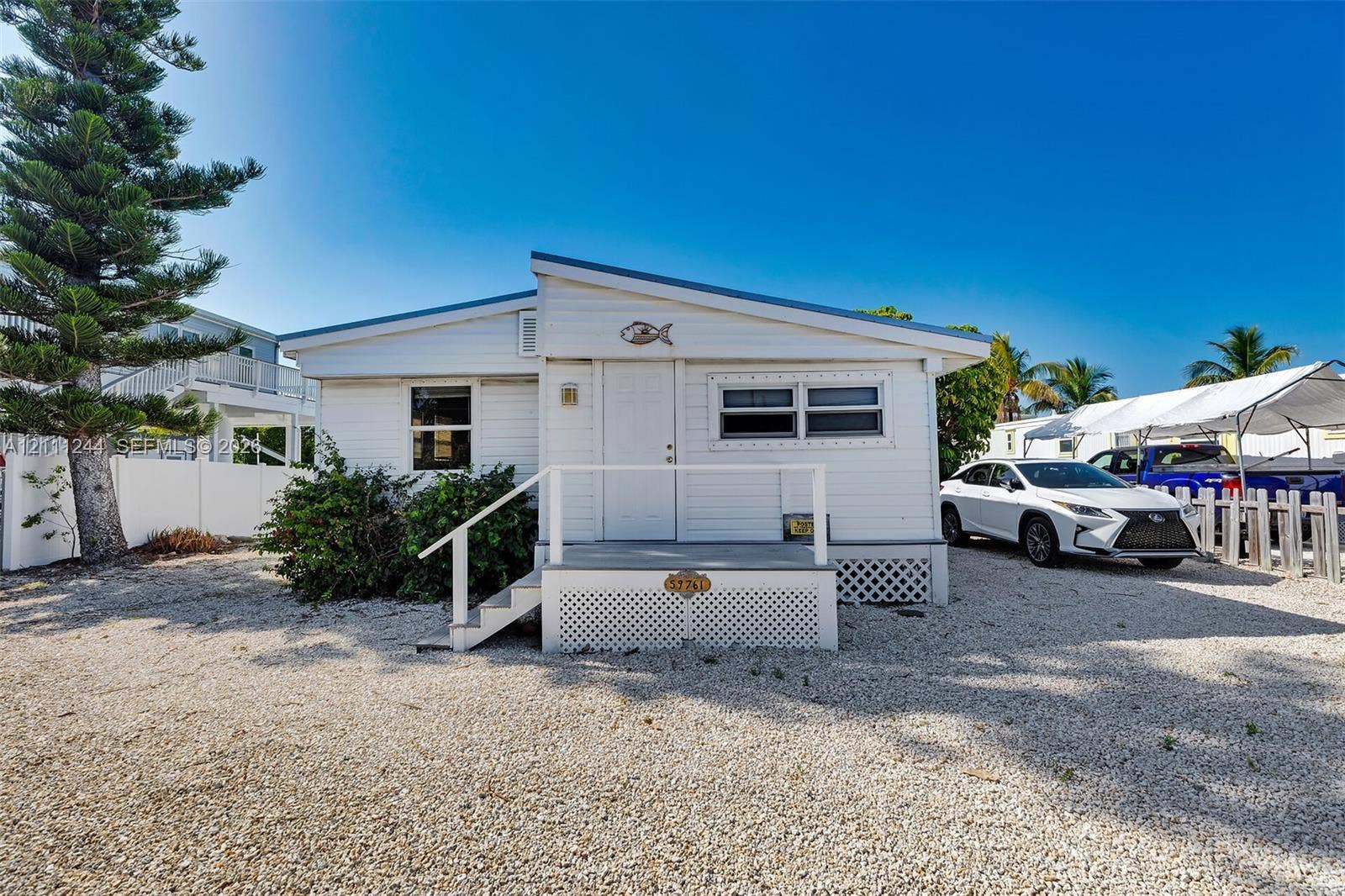 Single-story exterior featuring white horizontal siding, a shed-style roofline, an elevated front entry porch with white railings, and a lattice-skirted foundation