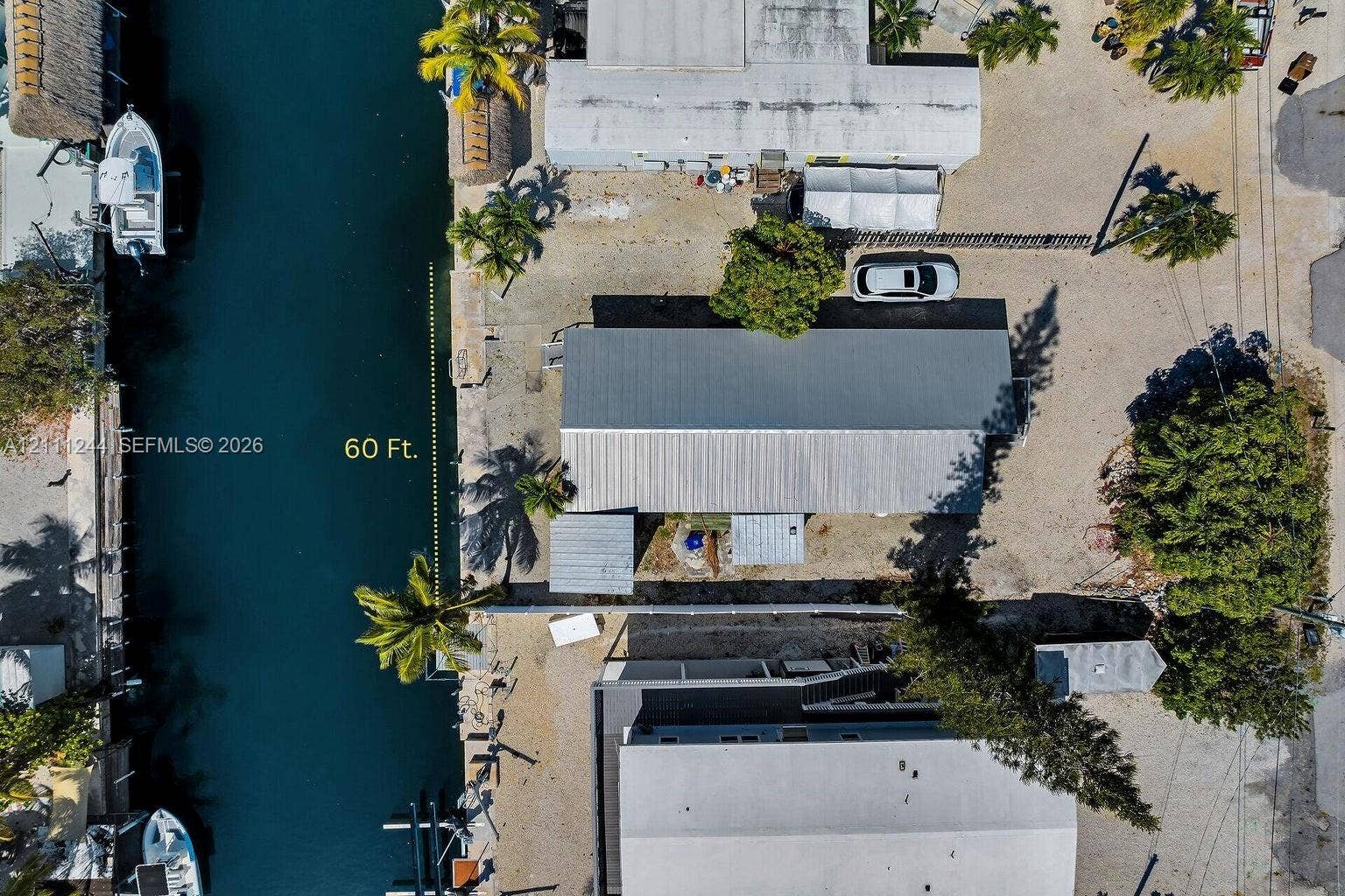 Aerial perspective of a waterfront property featuring 60 feet of canal frontage, a metal roof structure, and mature palms