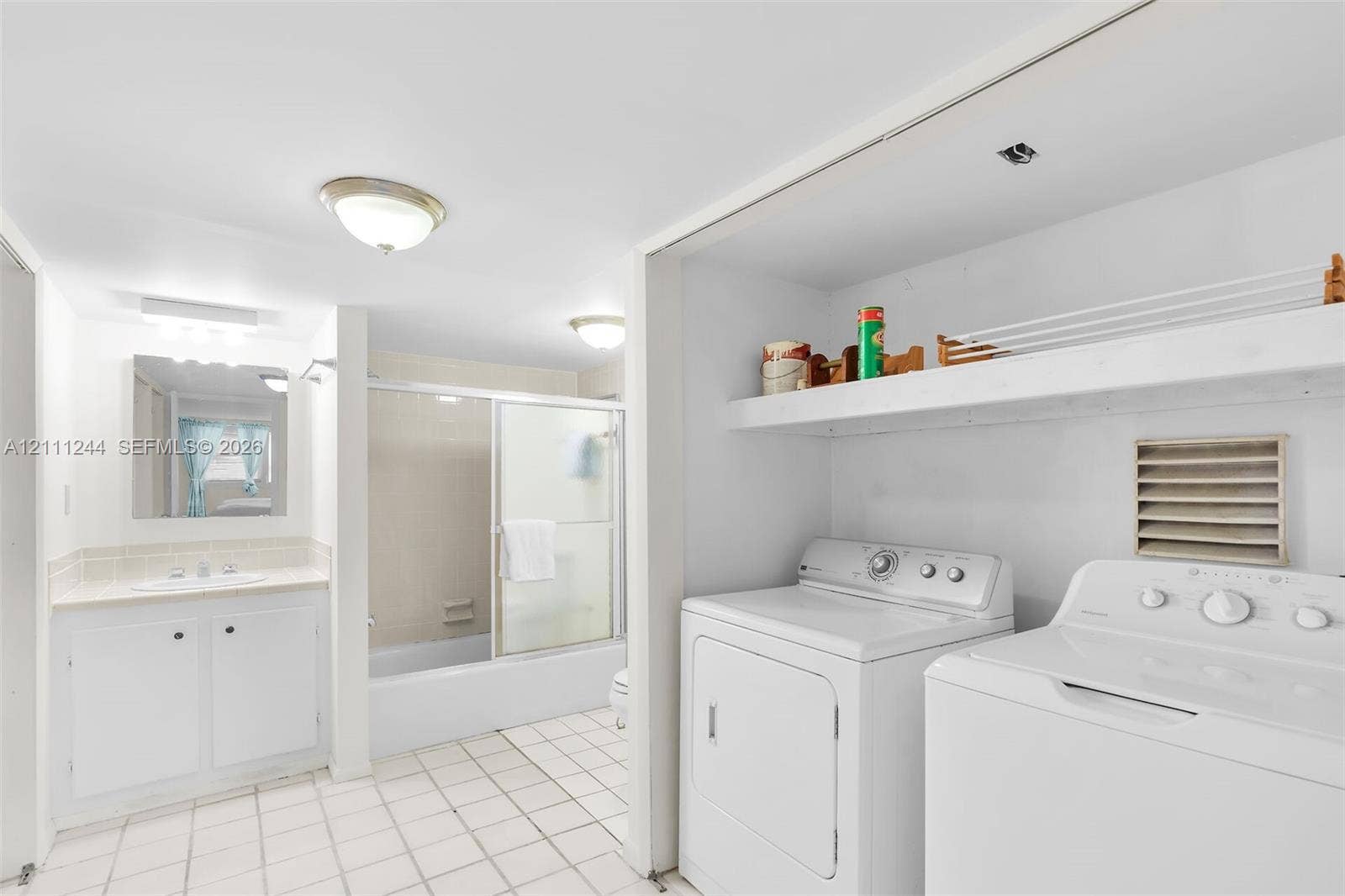 Bathroom featuring a vanity with integrated sink, tub-shower combination with sliding glass doors, ceramic tile flooring, and a dedicated laundry area with built-in shelving