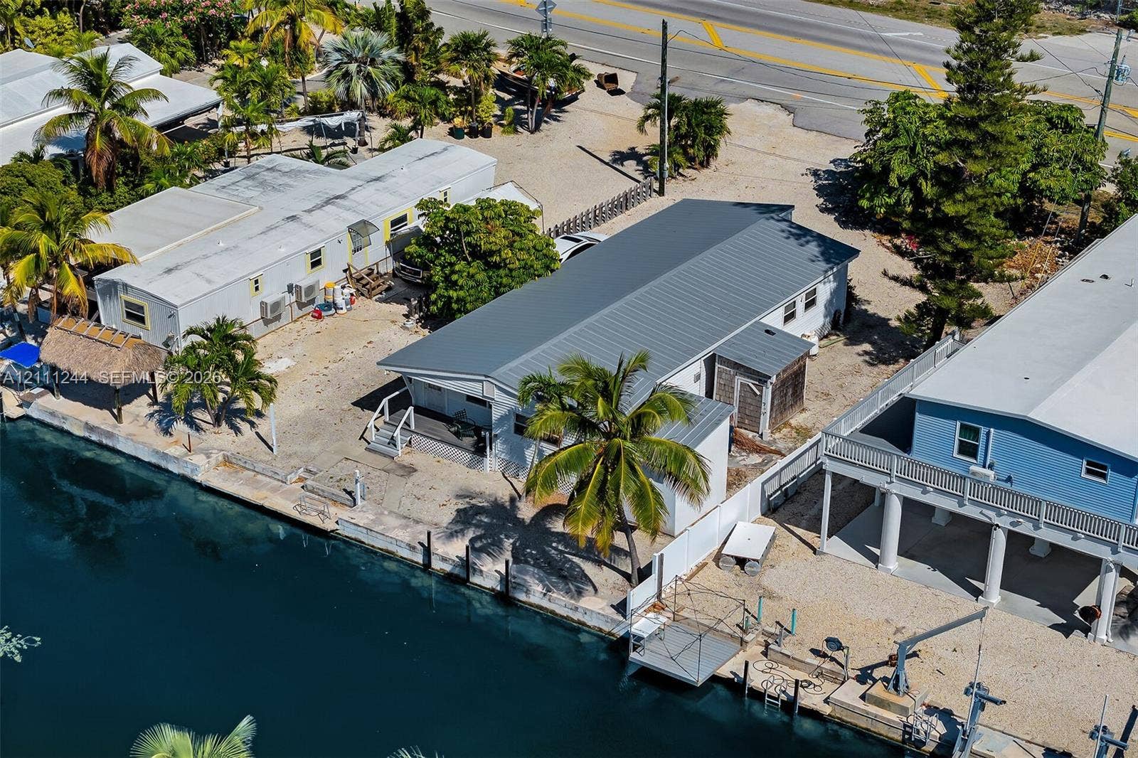 Waterfront property featuring a metal roof, private dock, sea wall, and mature palm trees