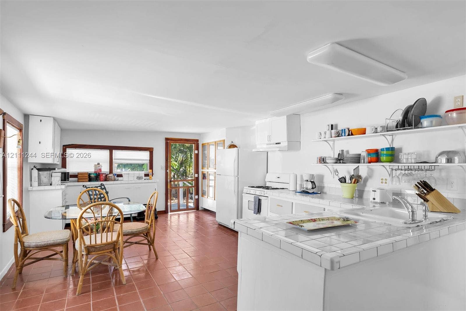 Kitchen featuring tile countertops, white cabinetry, open shelving, tile flooring, and a screen door