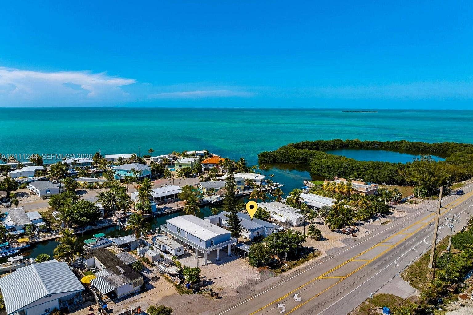 Aerial perspective of a coastal property featuring waterfront access, elevated structural design, gravel lot, and proximity to open water
