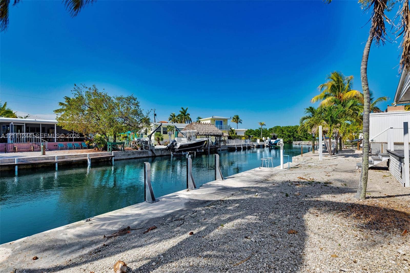 Waterfront property featuring a concrete seawall, private boat slip, gravel grounds, and mature palm trees