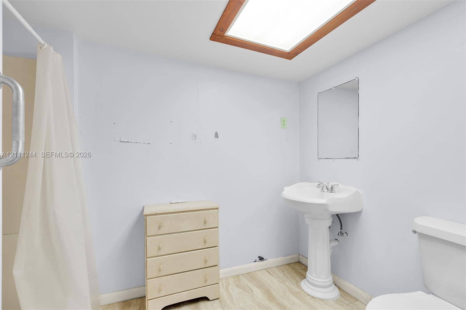 Bathroom featuring a ceiling skylight with a wood frame, pedestal sink, wall-mounted mirror, and wood-finish flooring