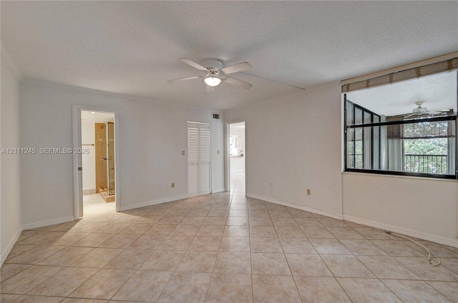 6800 Cypress Road, #506, Plantation, FL 33317 Room featuring large-format diagonal tile flooring, ceiling fan with integrated light fixture, louvered closet doors, and a multi-pane window with exterior greenery