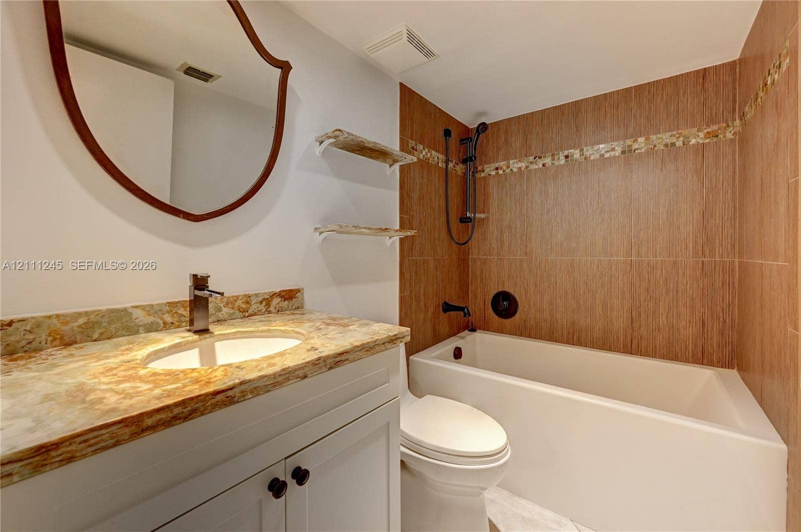6800 Cypress Road, #506, Plantation, FL 33317 Bathroom vanity featuring a stone countertop with integrated sink, wood-finish wall tile surrounding the bathtub, matte black fixtures, and a wall-mounted mirror