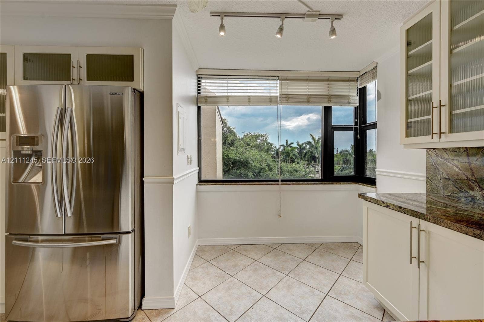 6800 Cypress Road, #506, Plantation, FL 33317 Kitchen featuring stainless steel French door refrigerator, white cabinetry with glass-front uppers, stone-finish countertops, tile flooring, and track lighting