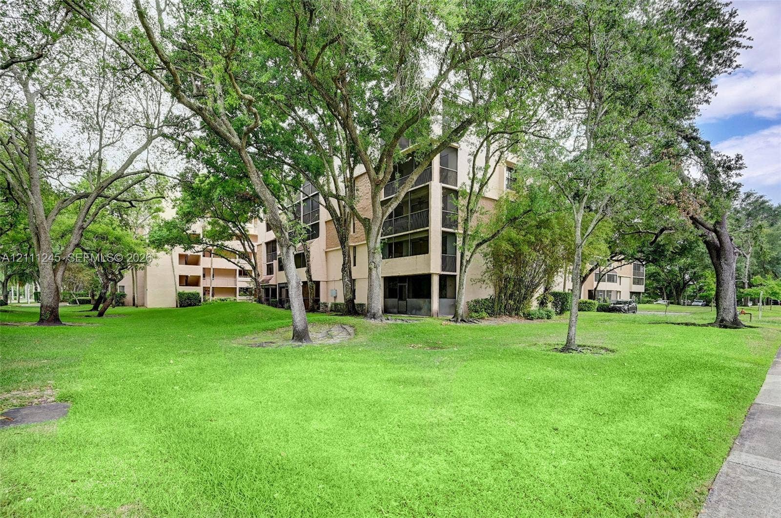 6800 Cypress Road, #506, Plantation, FL 33317 Multi-story building exterior featuring screened balconies, stucco siding, and surrounding mature trees over a landscaped lawn