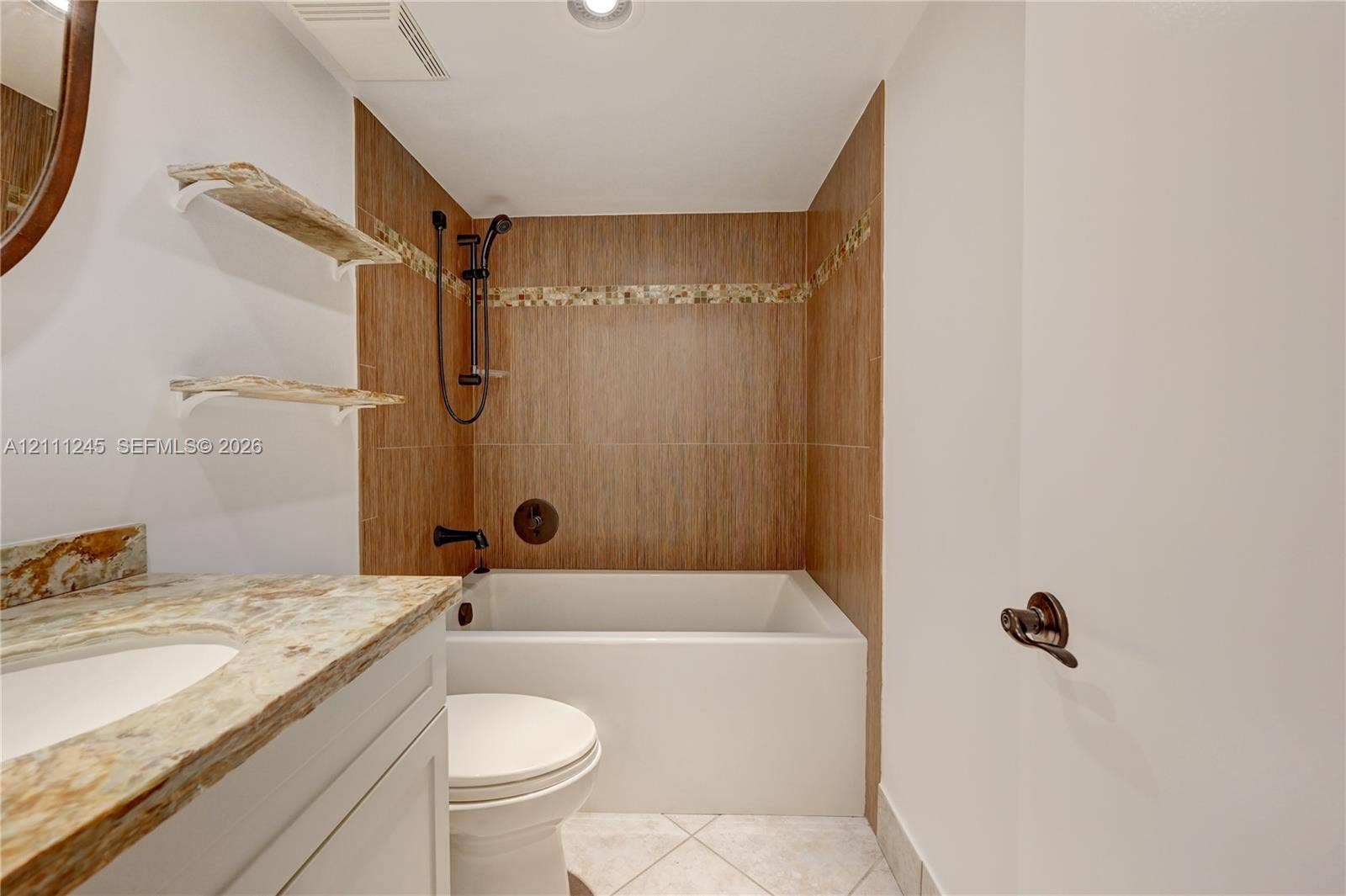 6800 Cypress Road, #506, Plantation, FL 33317 Bathroom featuring a vanity with a natural stone countertop, wall-mounted floating wood shelves, and a deep-soaking bathtub with wood-finish tile surround and matte black fixtures