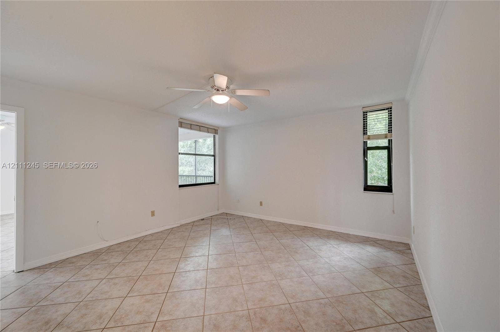 6800 Cypress Road, #506, Plantation, FL 33317 Interior space featuring neutral-toned tile flooring, white wall finishes, a central ceiling fan with integrated lighting, and multiple windows with fixed treatments