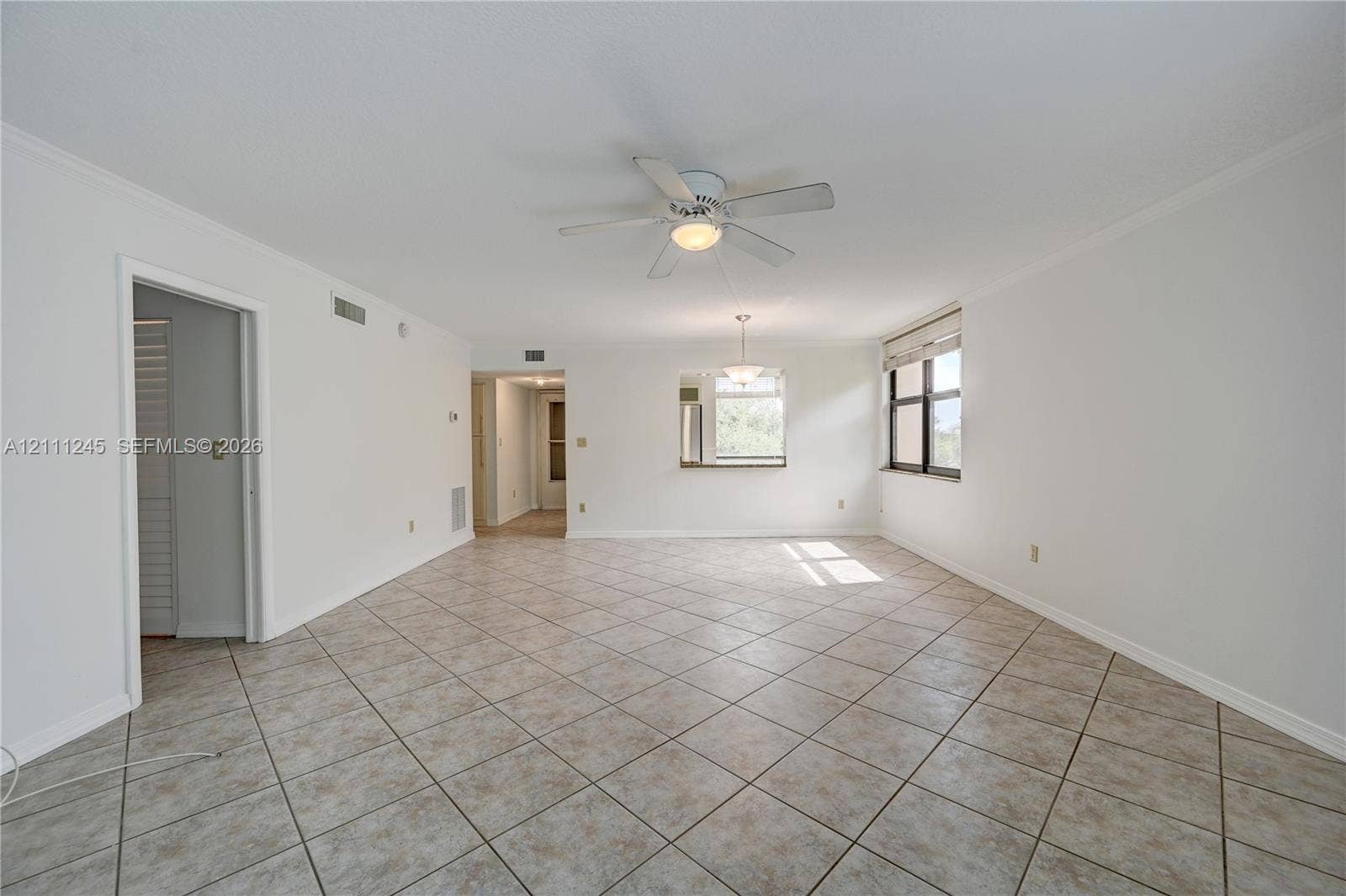 6800 Cypress Road, #506, Plantation, FL 33317 Open-concept interior featuring neutral tile flooring, a central ceiling fan with integrated lighting, a pass-through opening, and a large window with window treatments