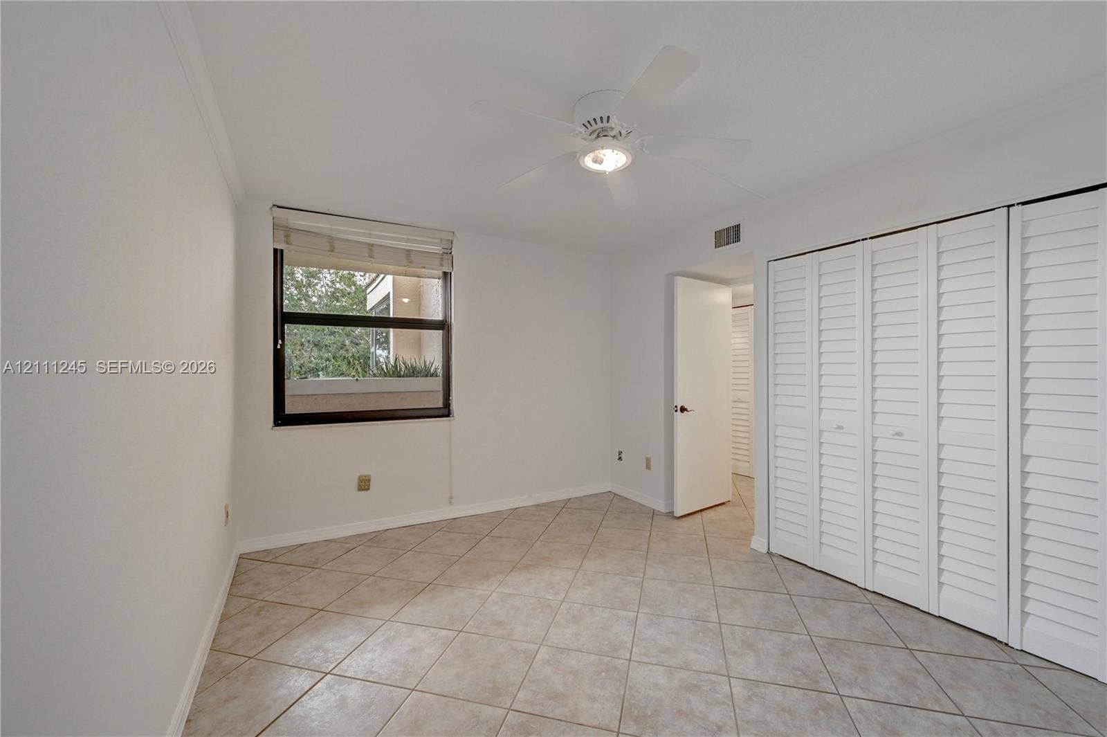 6800 Cypress Road, #506, Plantation, FL 33317 Neutral-toned tile flooring, white shutter-style closet doors, single-window illumination, and a ceiling-mounted fan with integrated lighting