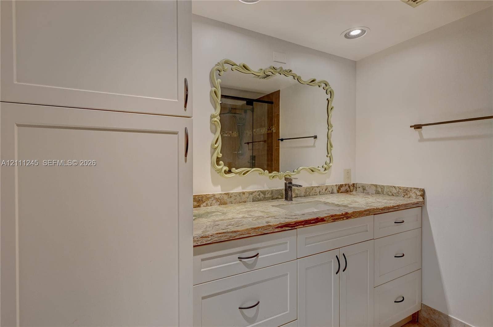 6800 Cypress Road, #506, Plantation, FL 33317 Bathroom vanity featuring white shaker-style cabinetry, multi-tonal stone countertop with an integrated sink, decorative framed wall mirror, and recessed ceiling lighting