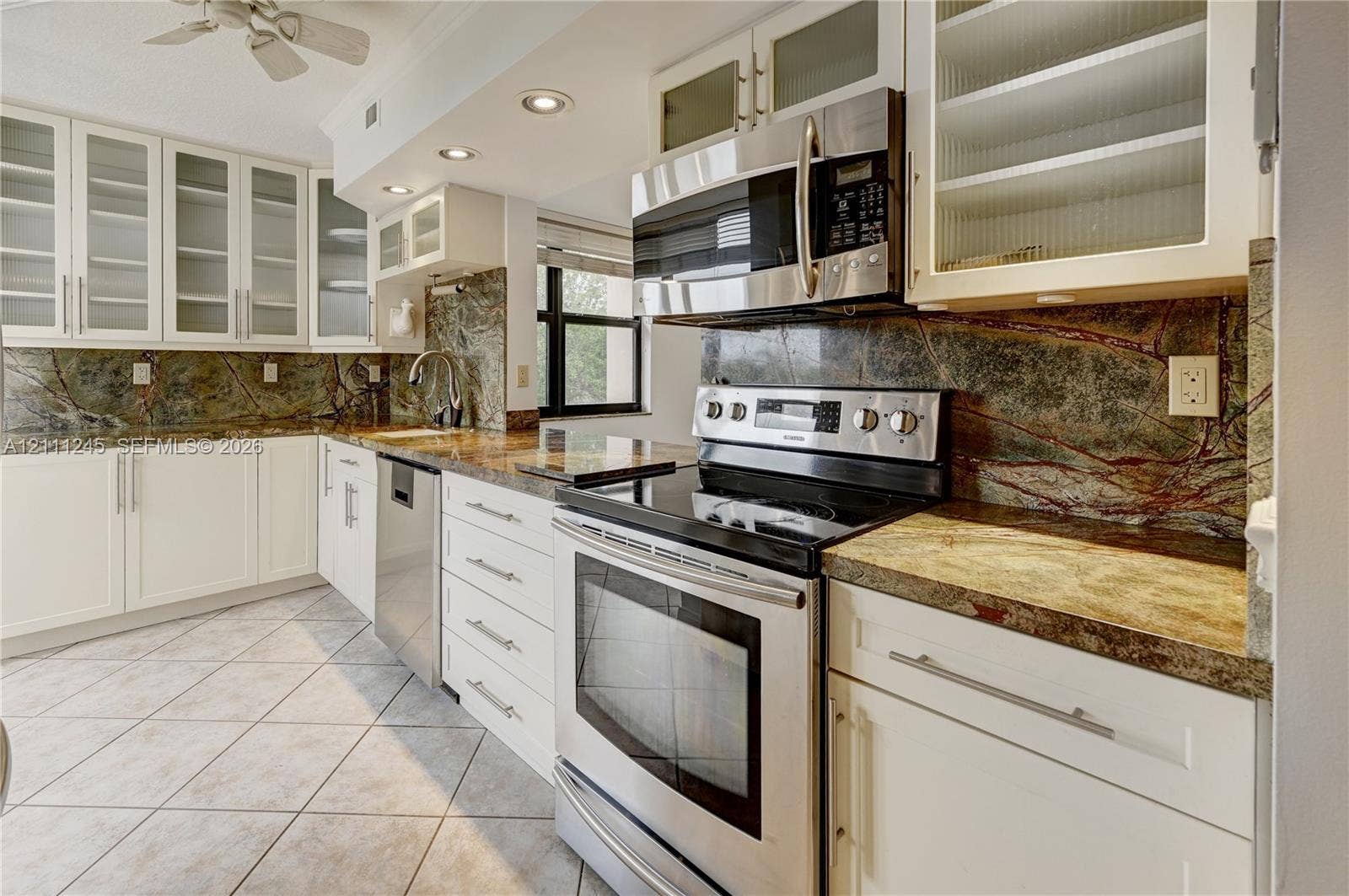 6800 Cypress Road, #506, Plantation, FL 33317 Kitchen featuring white shaker-style cabinetry with glass-front uppers, natural stone countertops, a continuous stone backsplash, stainless steel appliances, and diagonal tile flooring