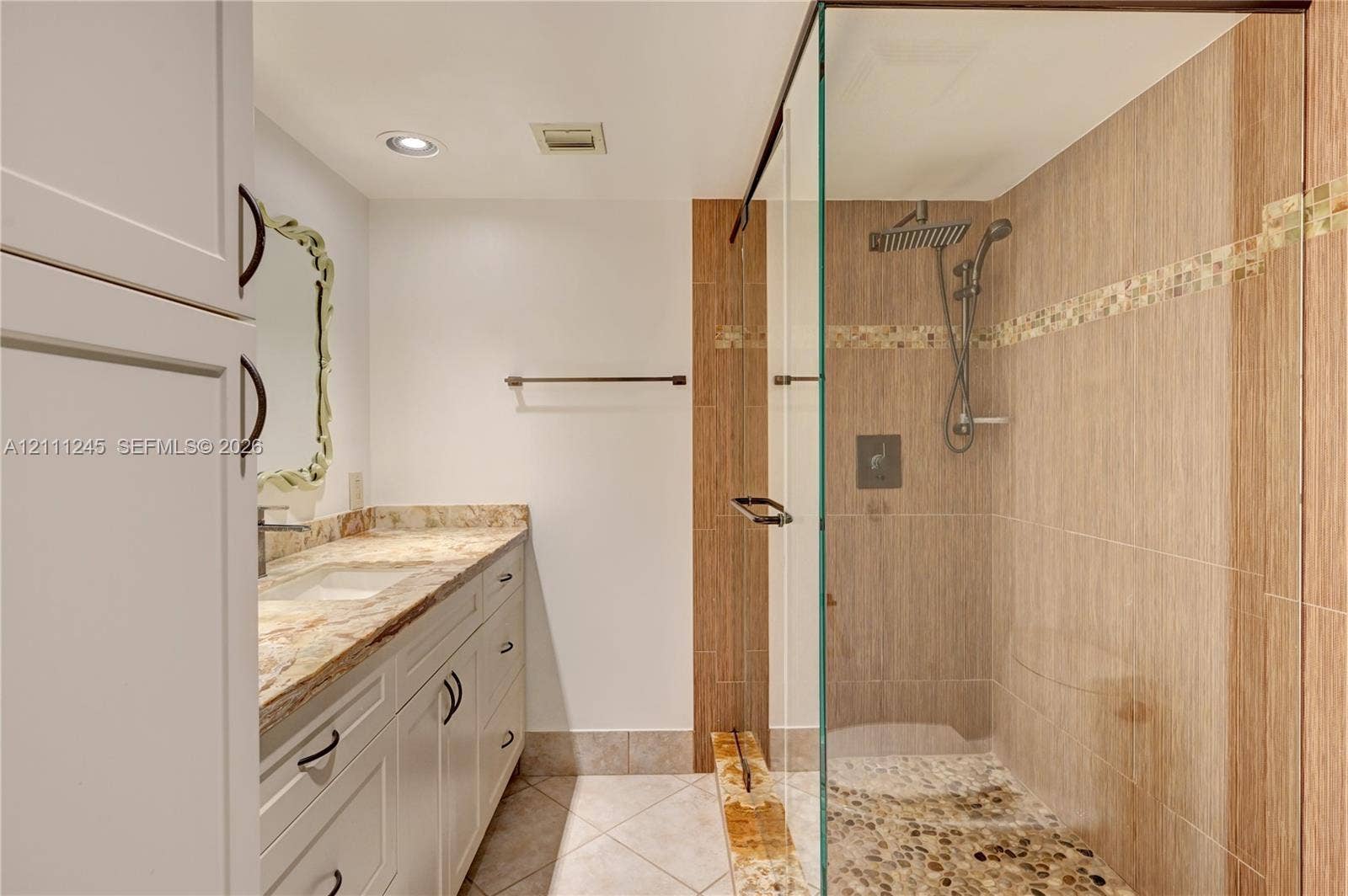 6800 Cypress Road, #506, Plantation, FL 33317 Bathroom featuring a white vanity with stone countertop, glass-enclosed shower with tiled walls, rainfall showerhead, and pebble-style shower flooring