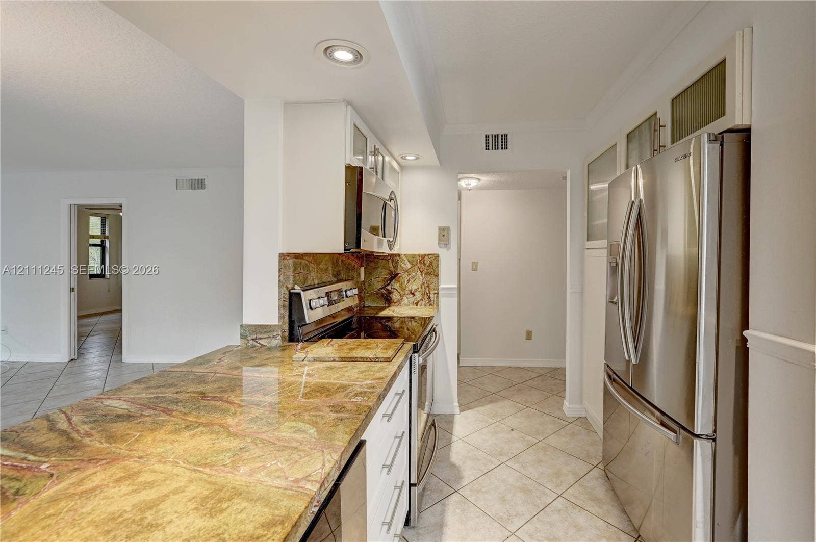 6800 Cypress Road, #506, Plantation, FL 33317 Kitchen featuring stone countertops, white cabinetry with glass-panel upper doors, stainless steel refrigerator, built-in microwave, and tile flooring
