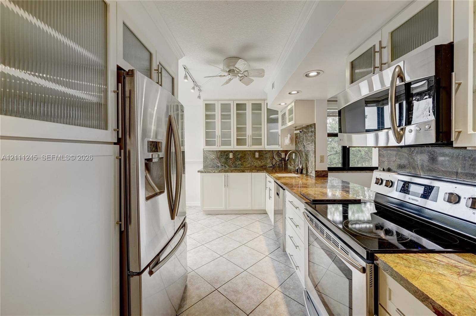 6800 Cypress Road, #506, Plantation, FL 33317 Kitchen featuring white cabinetry with glass-panel upper doors, stainless steel appliances, stone countertops, tiled backsplash, and stone-tile flooring