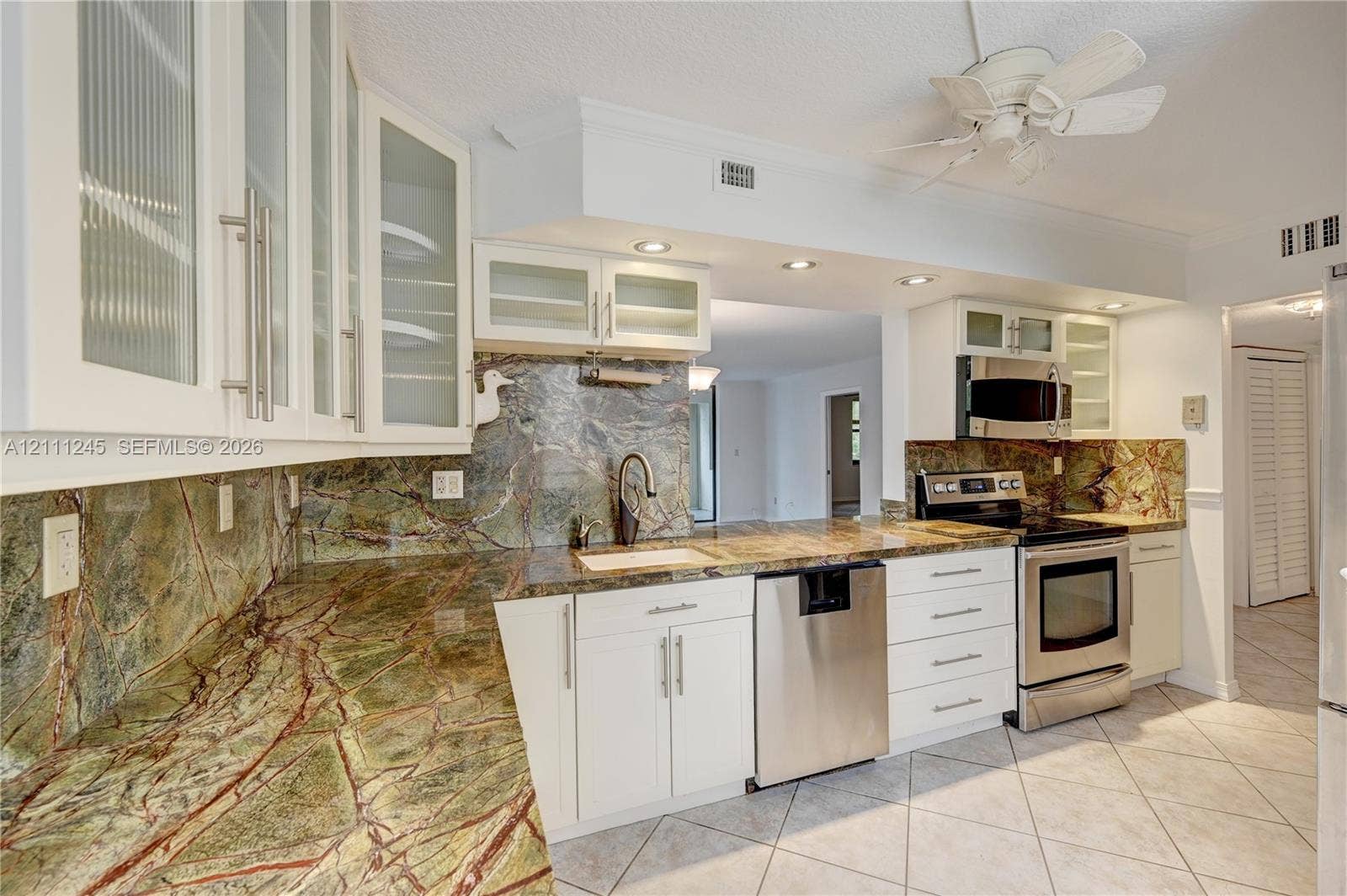 6800 Cypress Road, #506, Plantation, FL 33317 Kitchen featuring white shaker-style cabinetry with glass-front uppers, natural stone countertops, a full-height stone backsplash, stainless steel appliances, and tile flooring
