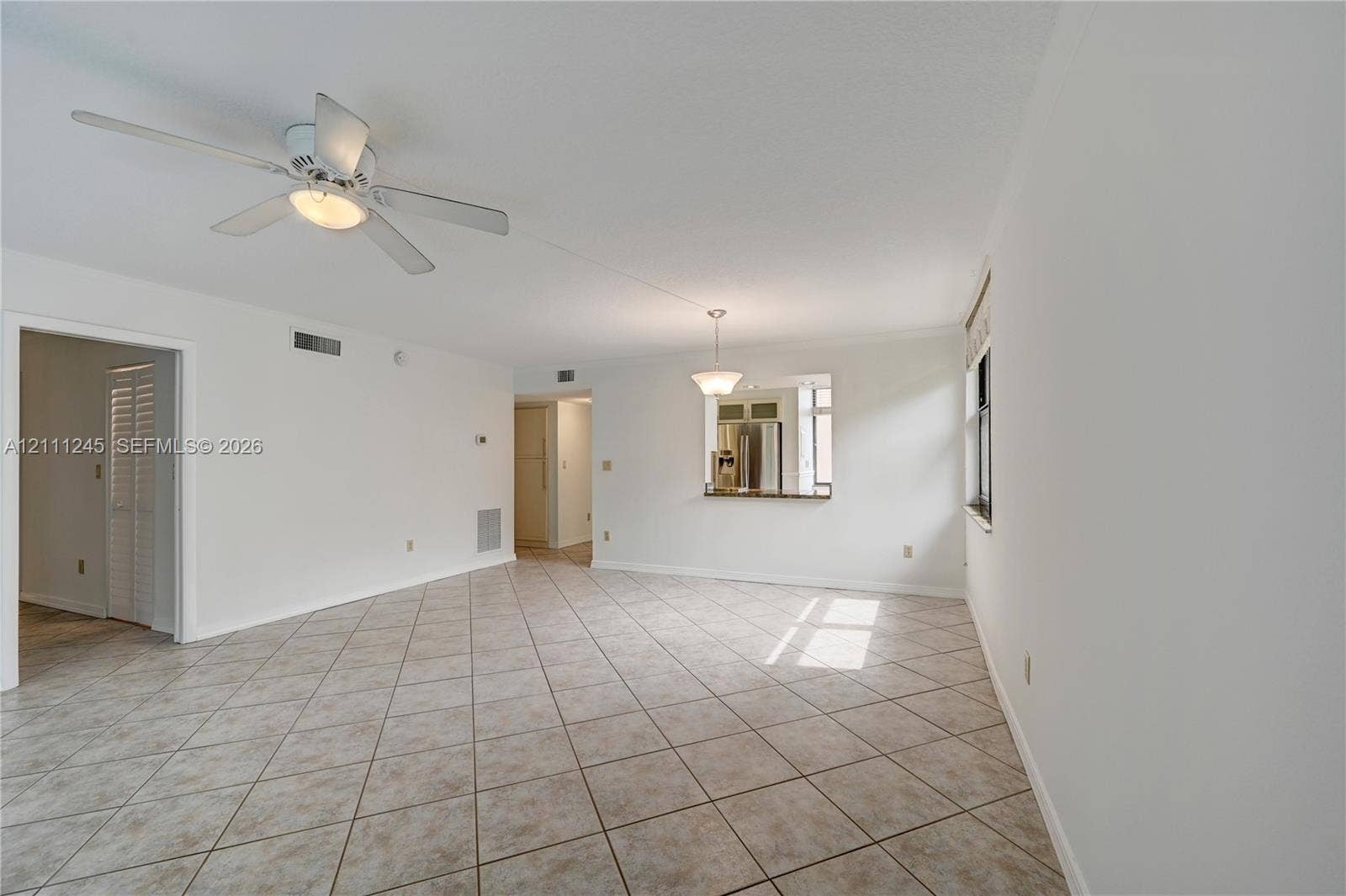 6800 Cypress Road, #506, Plantation, FL 33317 Open-concept interior featuring neutral tile flooring, white walls, a ceiling fan with integrated lighting, and a kitchen pass-through window with an attached counter