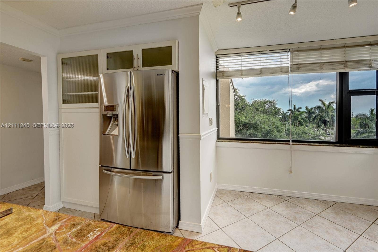 6800 Cypress Road, #506, Plantation, FL 33317 Kitchen featuring built-in cabinetry with glass-front upper panels, stainless steel French-door refrigerator, large-format tile flooring, multi-directional track lighting, and a window with exterior greenery