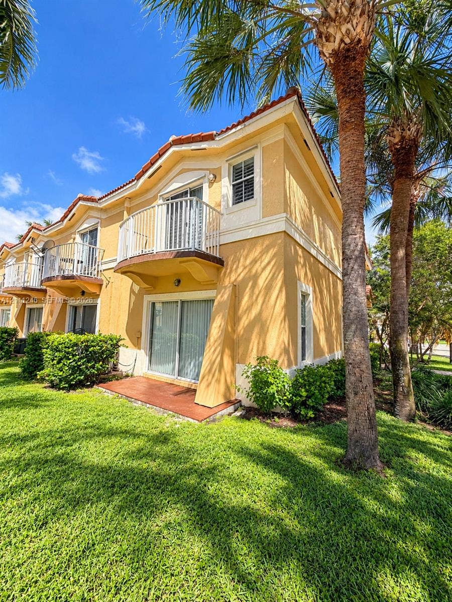 Multi-story exterior featuring stucco siding, a tiled roof, second-level balconies with metal railings, sliding glass doors, and a ground-level patio