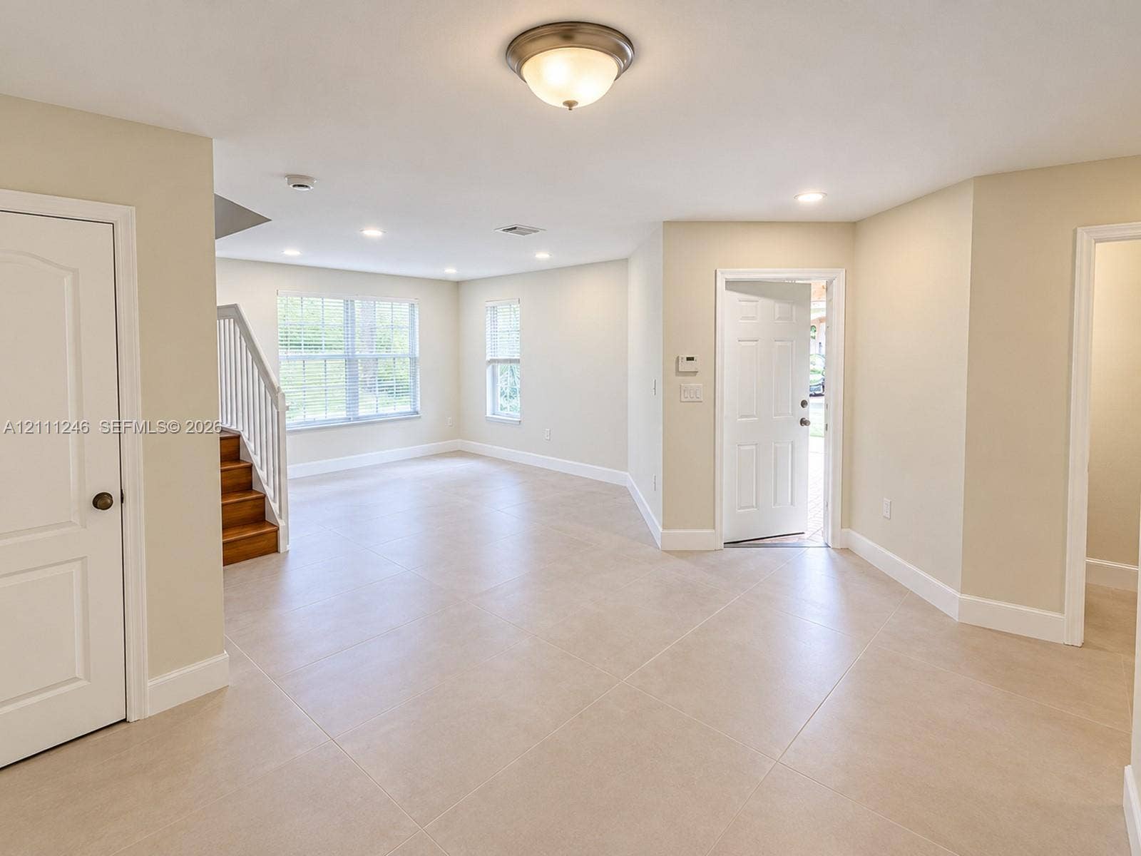 Neutral tile flooring, recessed lighting, double-hung windows, and a wood-tread staircase with white balusters