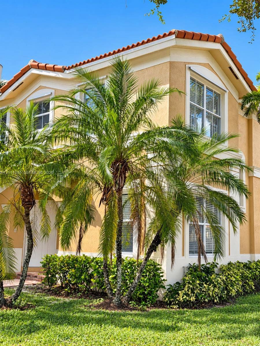 Stucco exterior featuring a multi-gabled terracotta tile roof, white trim accents, and mature palm tree landscaping