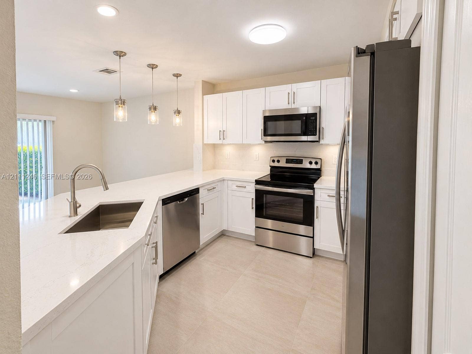 Kitchen featuring white shaker-style cabinetry, solid-surface countertops, stainless steel appliances, a peninsula with an undermount sink, and light-toned tile flooring