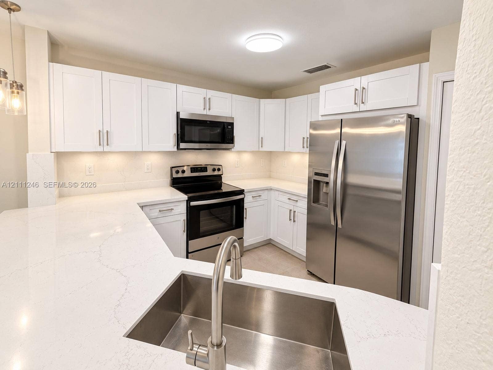 Kitchen featuring white shaker-style cabinetry, white countertops with grey veining, stainless steel appliances, and an undermount stainless steel sink with a high-arch faucet