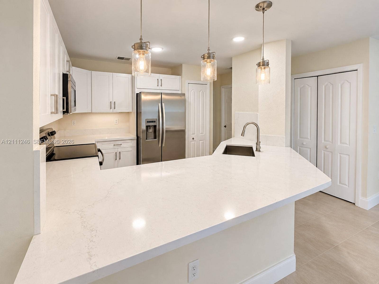 Kitchen featuring white cabinetry, quartz countertops, stainless steel appliances, a peninsula with an undermount sink, and three glass pendant lights