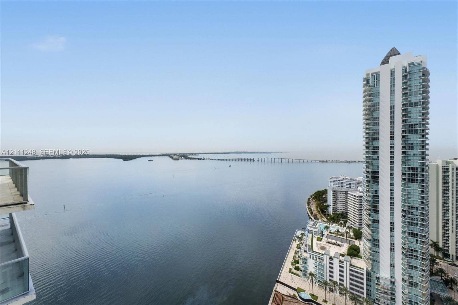 High-rise balcony with a metal railing overlooking a large bay, coastal causeway, and metropolitan skyline