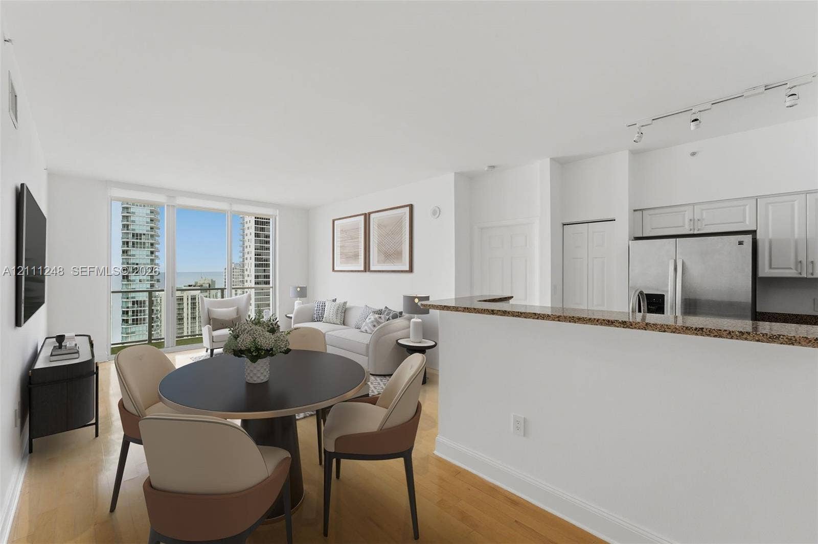 Open-concept living space featuring wood-finish flooring, floor-to-ceiling windows, and a kitchen peninsula with a stone-finish countertop