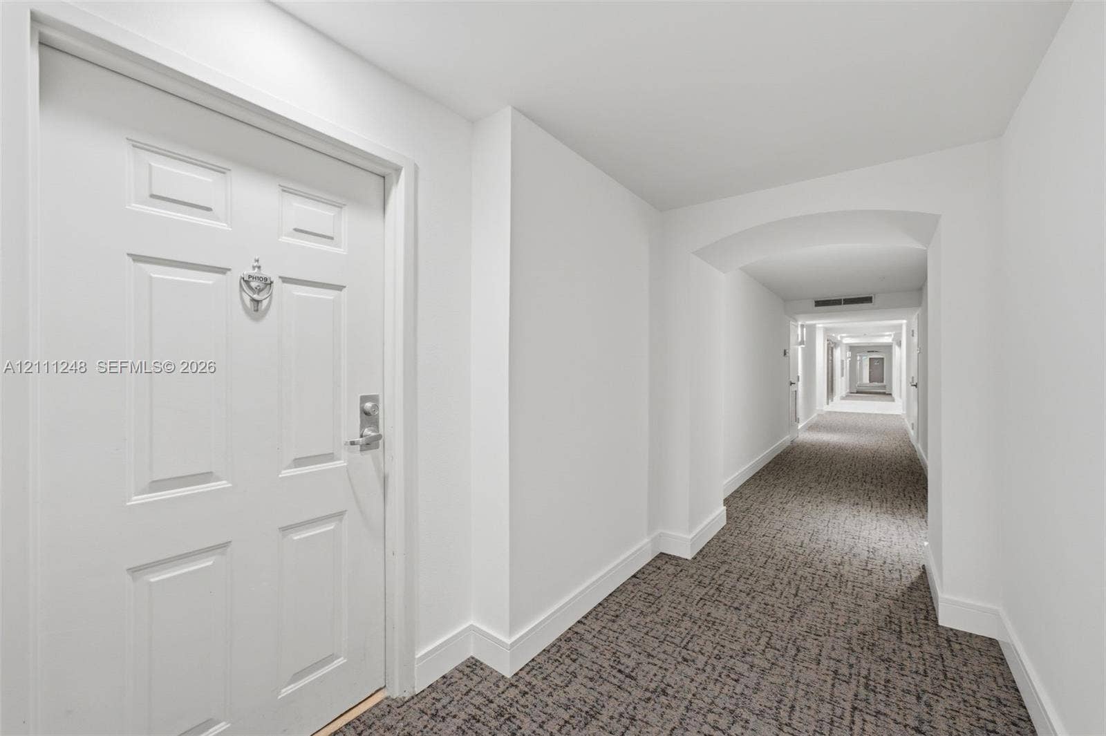 Paneled entry door with metal hardware and patterned carpeting throughout the hallway