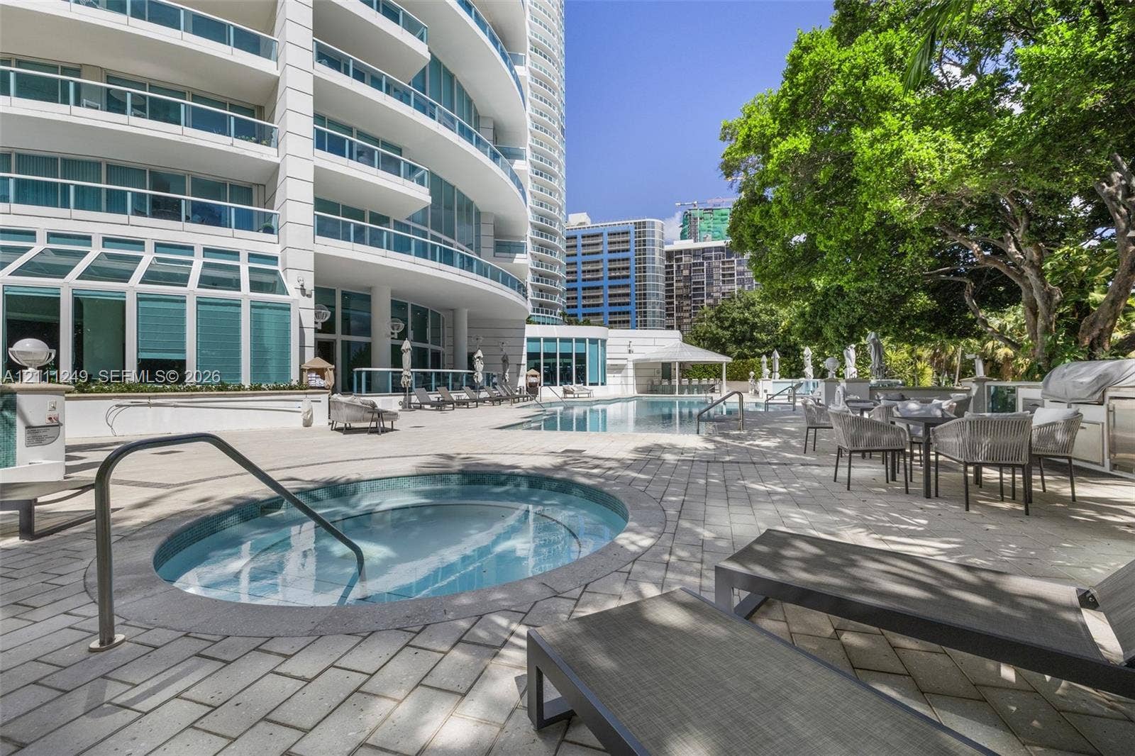 Outdoor pool terrace featuring a circular in-ground spa, stone paver decking, and mature trees