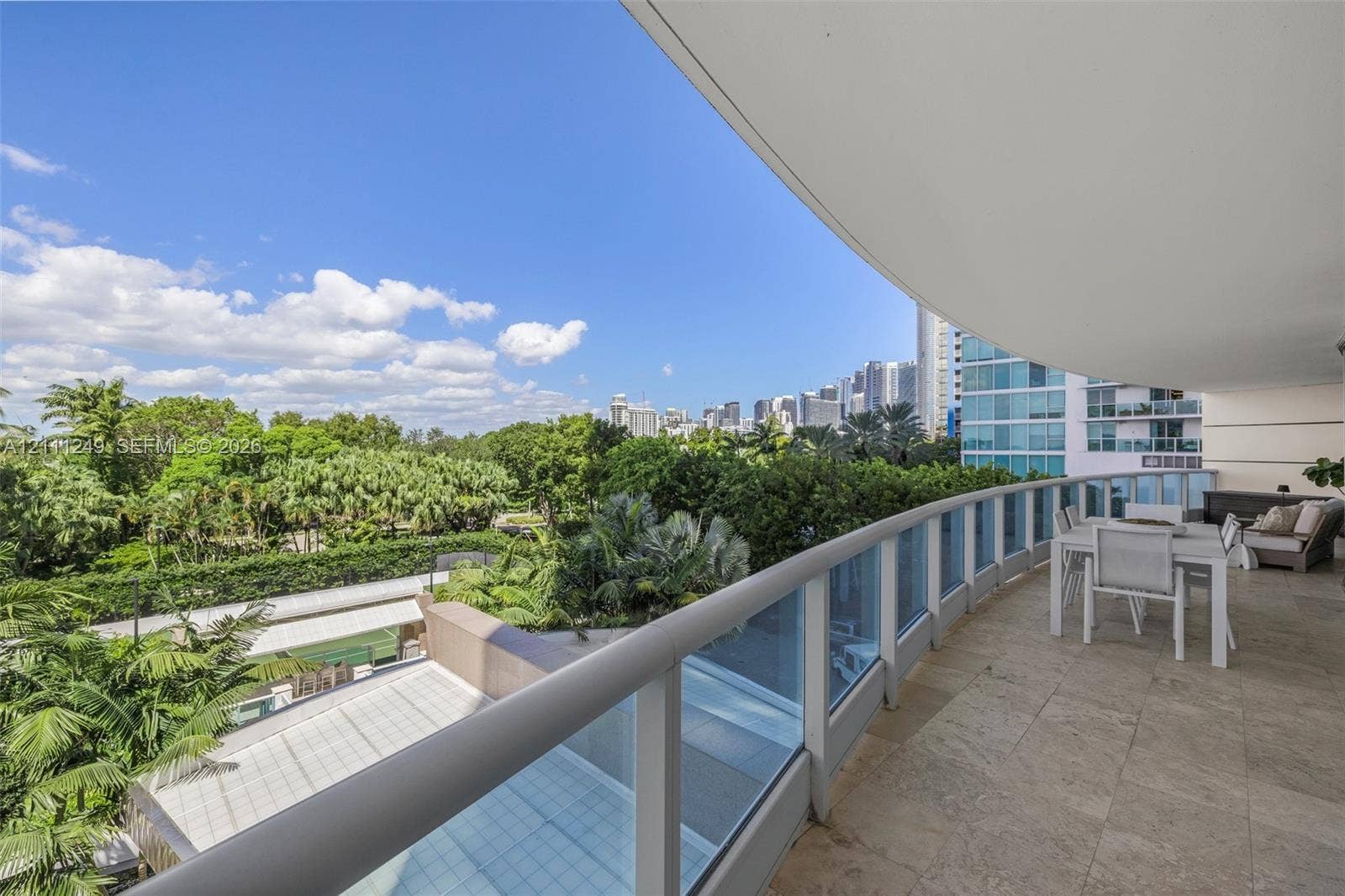 Expansive covered balcony featuring stone tile flooring and glass panel railings with metal framing