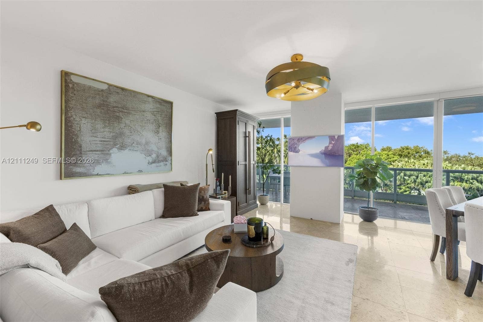 Living area featuring large-format stone flooring, floor-to-ceiling glass windows, a brass-finish contemporary chandelier, and a private balcony with natural scenery