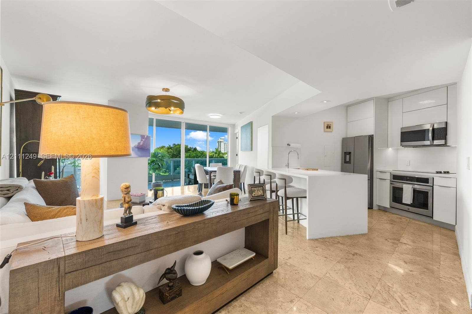 Open concept interior featuring stone-tile flooring, sleek white flat-panel cabinetry, a stainless steel appliance suite, and a waterfall-edge kitchen island
