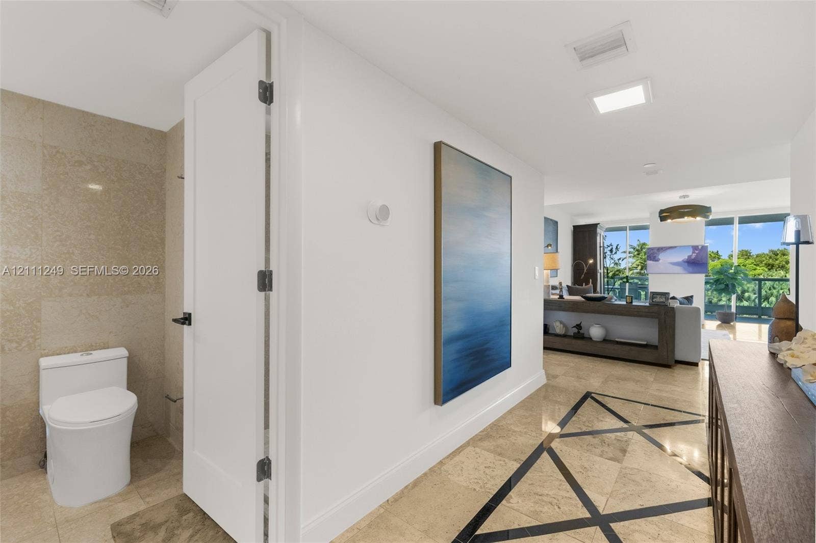 Bathroom featuring a white integrated countertop and basin, high-gloss flat-panel cabinetry, large-format neutral wall tile, wall-to-wall mirror, and recessed ceiling lighting