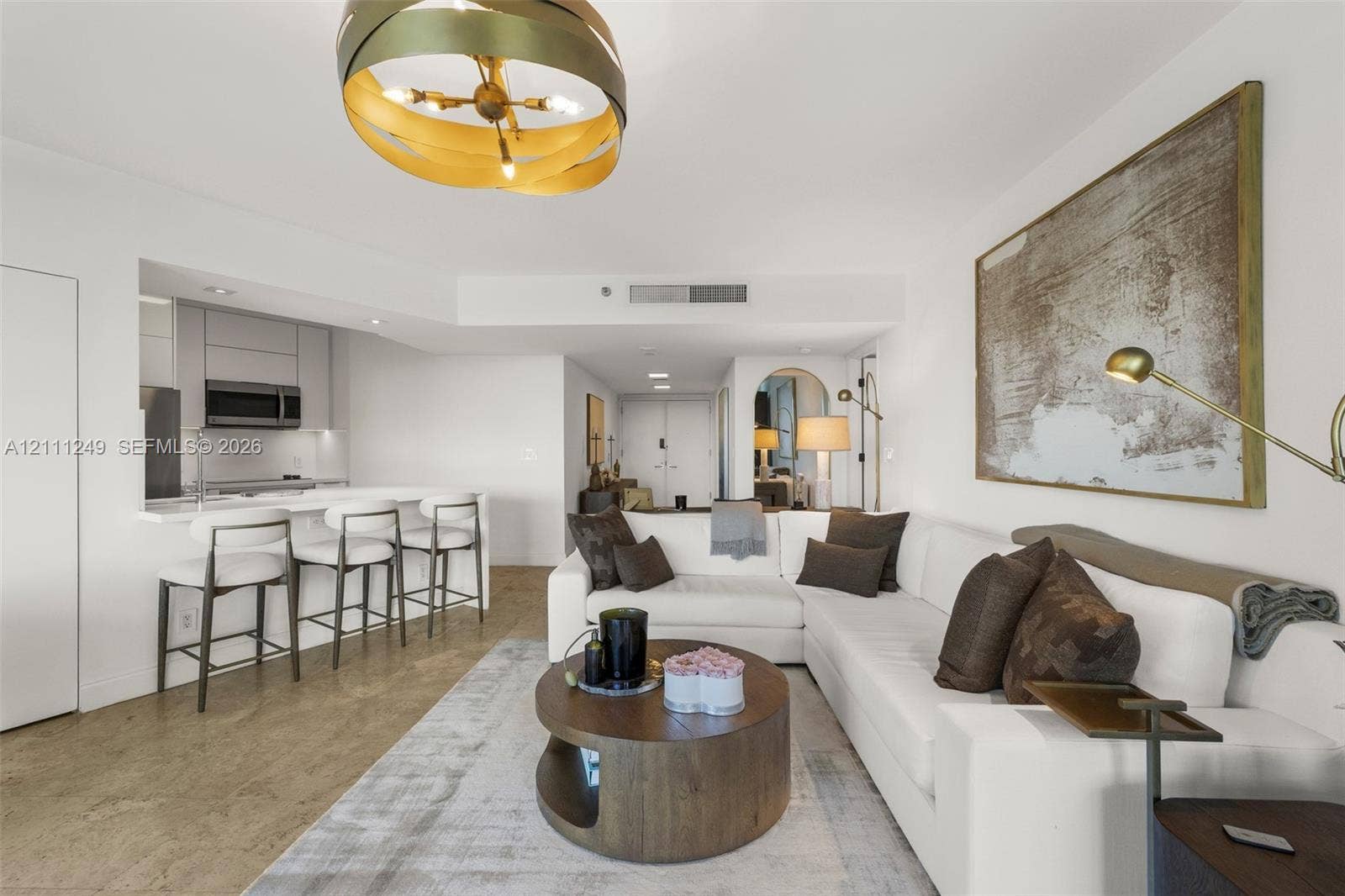 Open-concept living space featuring high-gloss cabinetry, a quartz waterfall-edge breakfast bar, polished concrete flooring, and a contemporary multi-tiered orb pendant light fixture