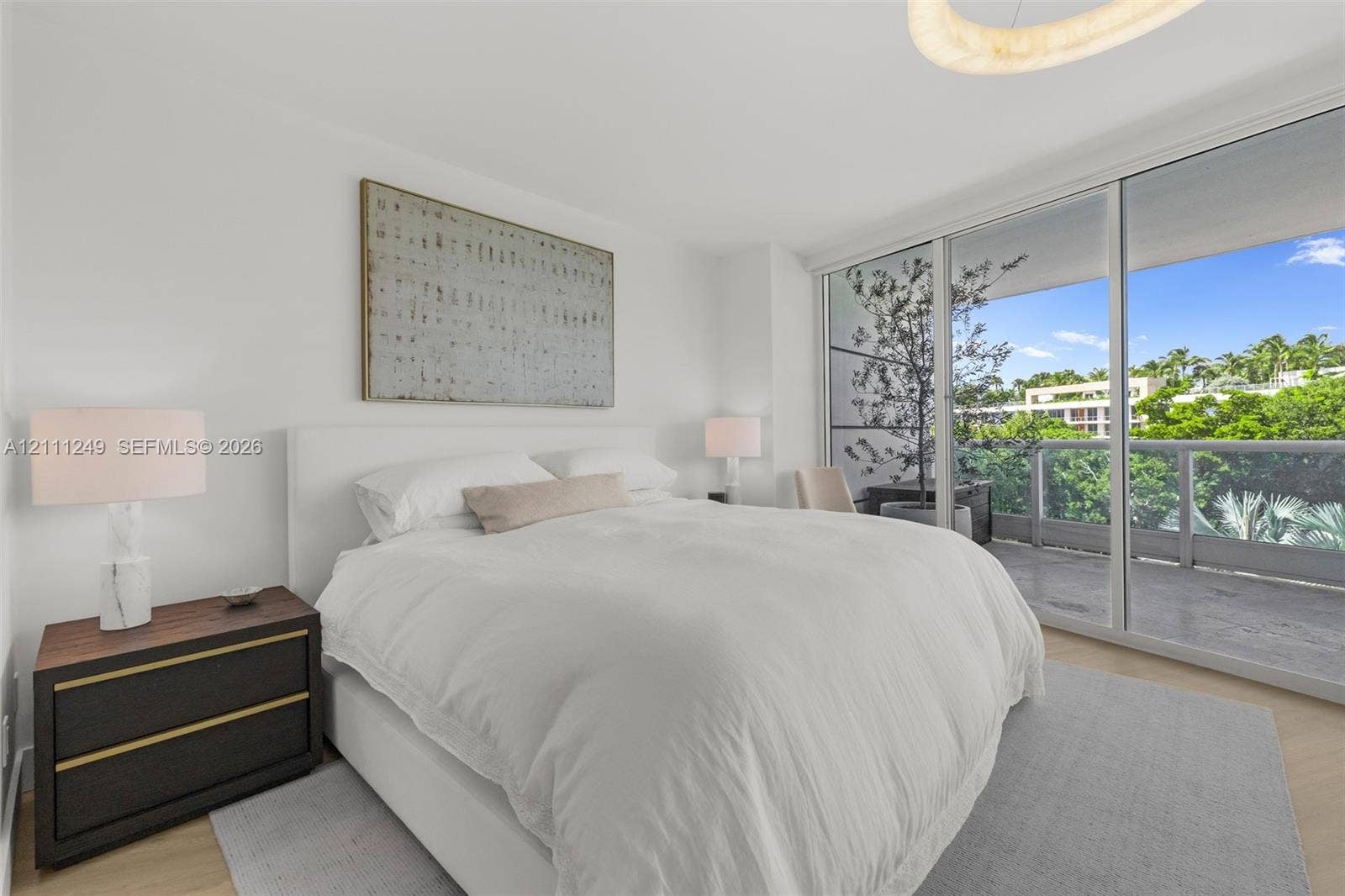 Floor-to-ceiling sliding glass doors, neutral interior walls, wood-finish flooring, and a glass-paneled balcony
