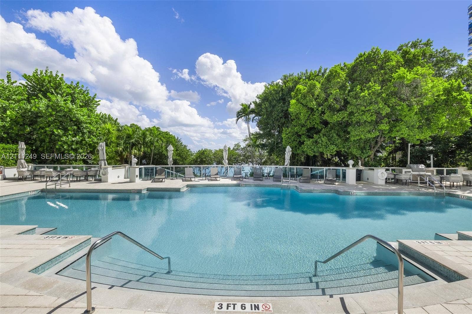 Swimming pool featuring a tiled deck, stone-finish coping, dual metal handrails, and a glass panel surround