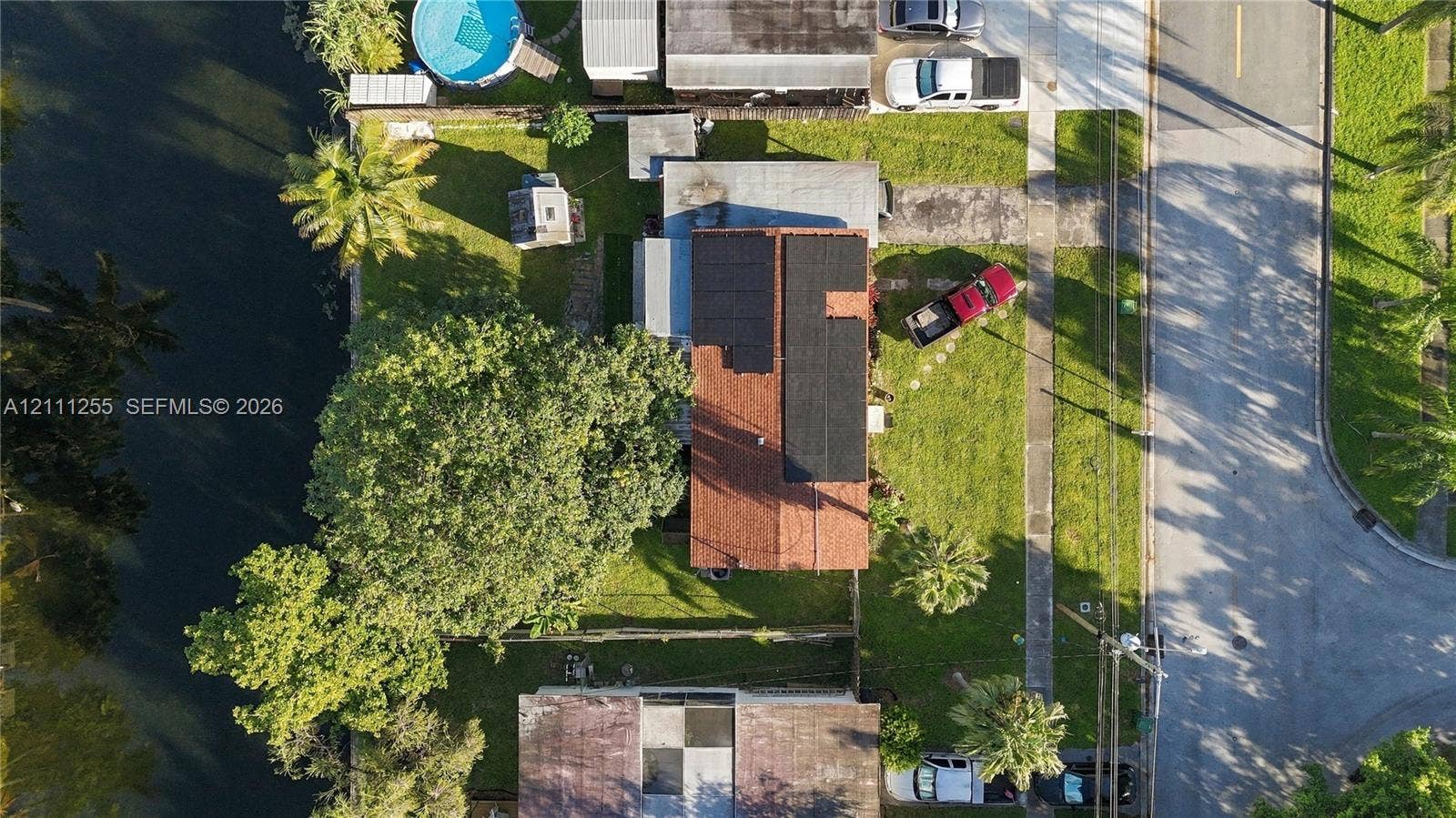 Aerial perspective featuring a property with roof-mounted solar panels, a paved driveway, and direct water frontage