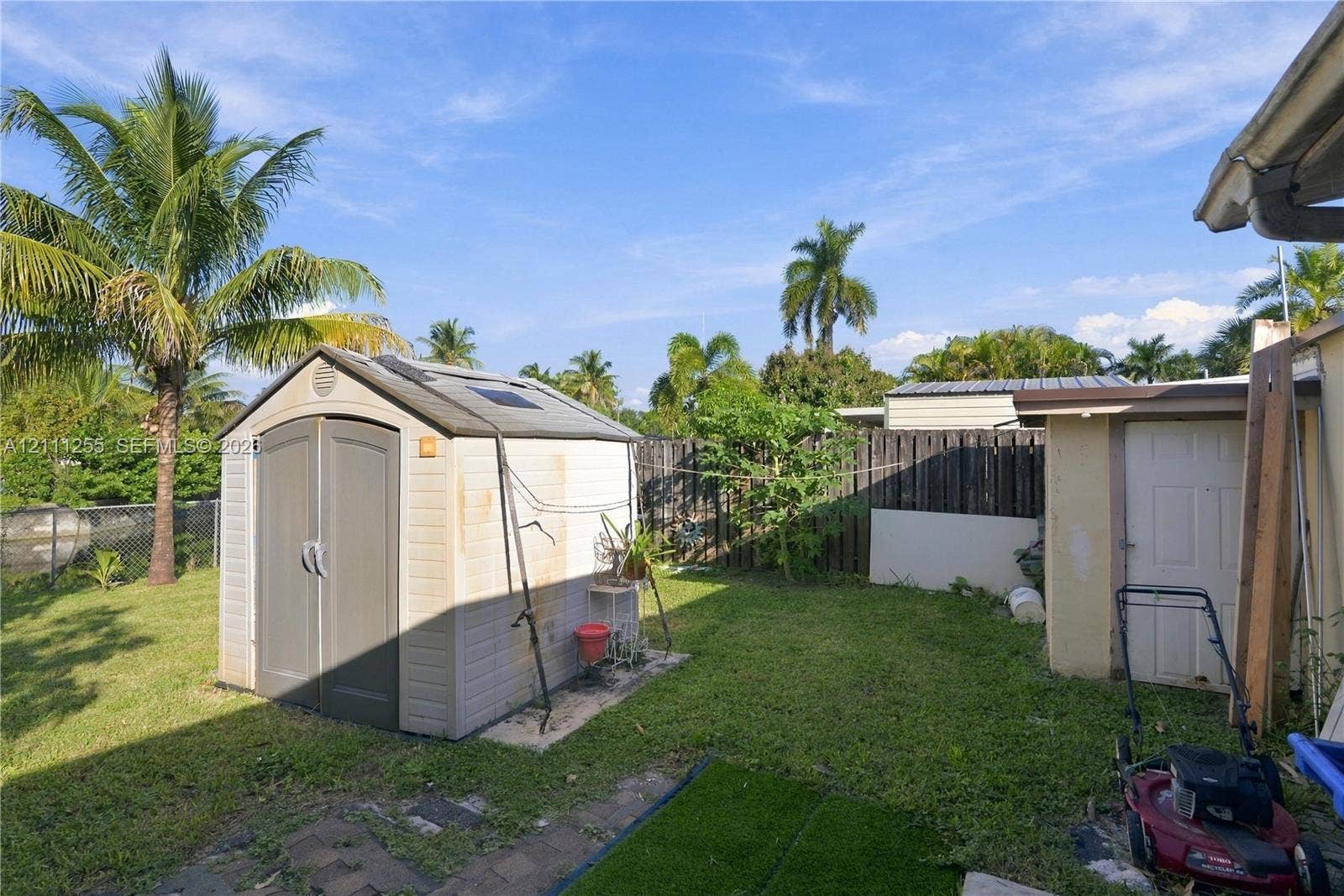 Backyard space featuring a standalone resin storage shed, a perimeter wood fence, and mature palm trees