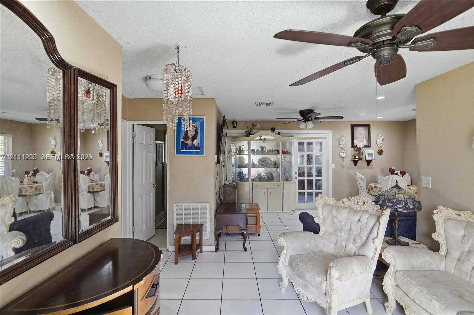 Interior featuring white ceramic tile flooring, tiered crystal chandelier, dual ceiling fans, and an arched-top wall mirror