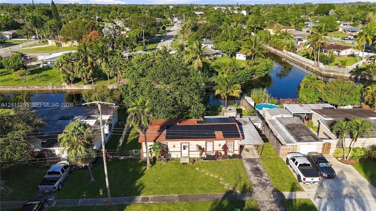 Single-story residence featuring a tile roof, roof-mounted solar panels, attached carport, and canal-front lot with mature landscaping