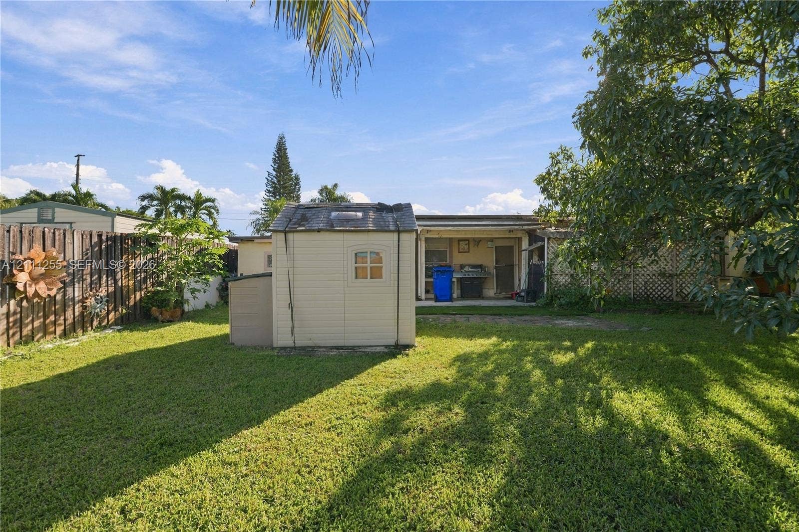 Backyard featuring a grass lawn, wood-panel fencing, mature trees, and a detached exterior storage structure