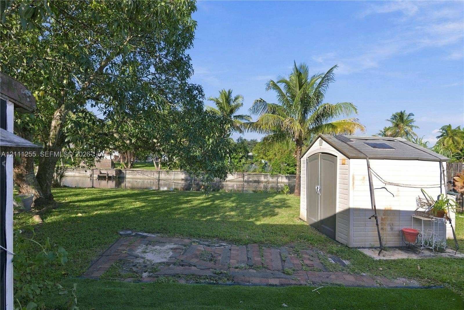 Backyard featuring a grass lawn, mature trees, a detached storage shed, a brick patio area, and a canal-front perimeter
