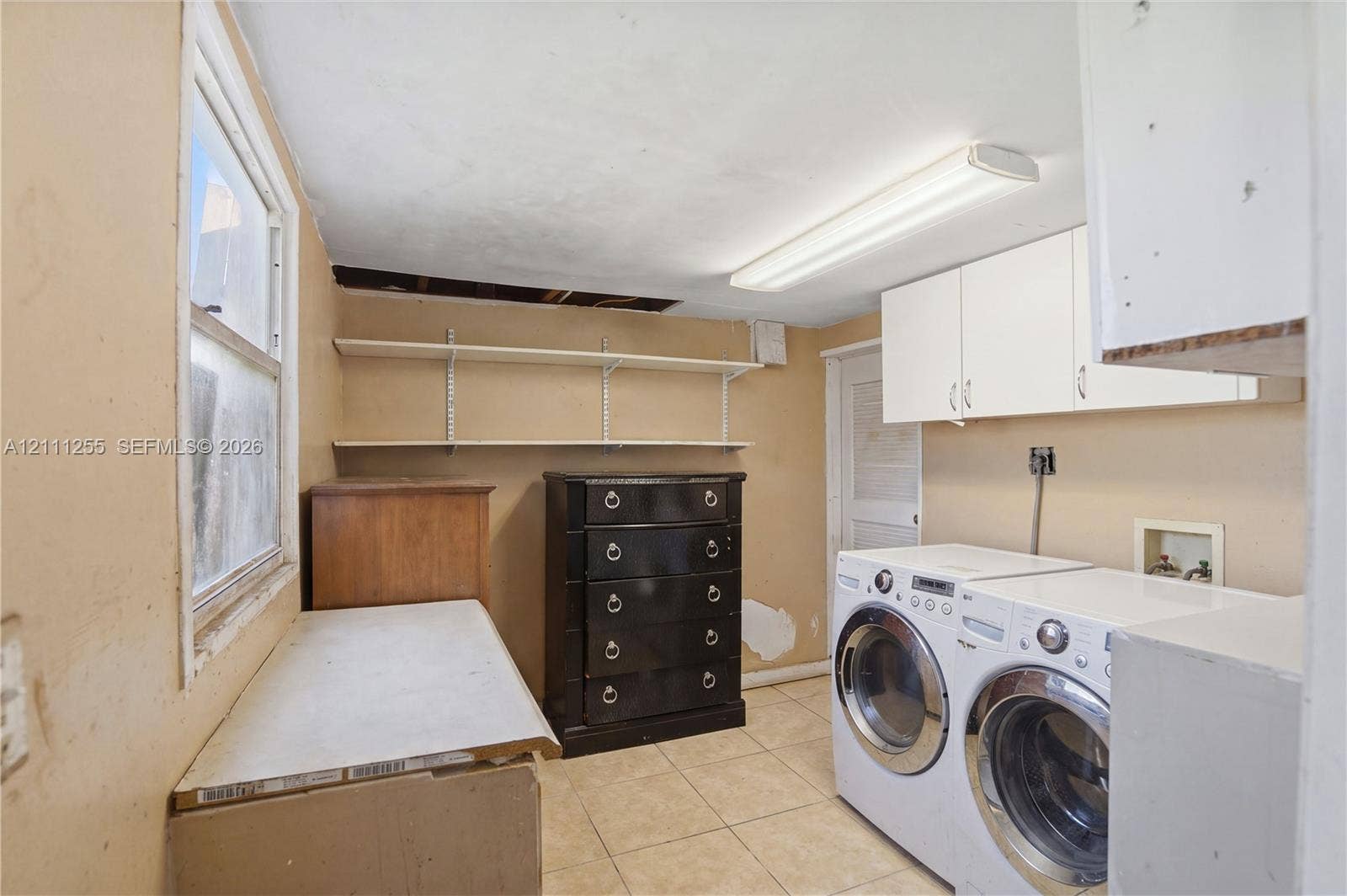Laundry space featuring wall-mounted upper cabinetry, open shelving, and tile flooring