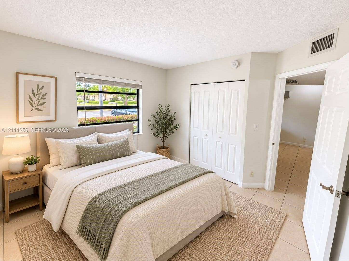 Neutral-toned interior space featuring light-colored tile flooring, a horizontal slider window, and built-in closet cabinetry with dual folding doors