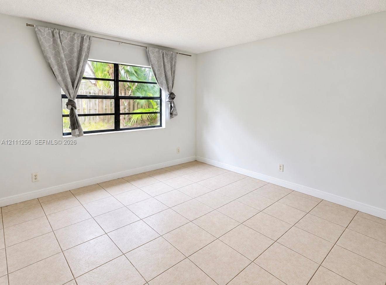 Neutral interior space featuring ceramic tile flooring, solid white walls, and a multi-pane window with a black frame